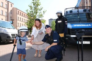 rodzina z dzieckiem przy stoisku policyjnym , maluch zakłada kask ochronny , obok policjant