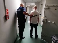 umundurowany policjant na korytarzu sprawdza zatrzymanego urządzeniem do wykrywania metalu