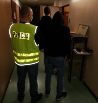 policjant w kamizelce odblaskowej stoi z zatrzymanym na korytarzu komendy