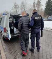 Policjanci wprowadzają do radiowozu zatrzymanego