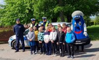 Dzieci wraz z maskotką policyjną - Komisarzem Błyskiem, policjantami ruchu drogowego i dzielnicowym pozują do współnego zdjęcia
