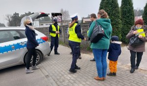 Policjanci wraz z pracownikiem Starostwa Powiatowego w Radomsku wręczają kamizelki odblaskowe w rejonie placu targowego w Przedborzu.