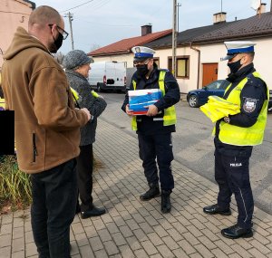 Policjanci wraz z pracownikiem Starostwa Powiatowego w Radomsku wręczają kamizelki odblaskowe w rejonie placu targowego w Kamieńsku.