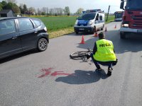 droga na której doszło do wypadku, widac hondę , plame krwi na jezdni i policjanta , który ogląda lezący na jezdni rower. w tle wóz strażacki