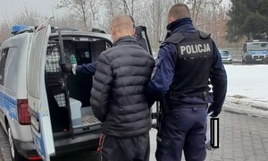 umundurowany policjant prowadzi zatrzymanego mężczyznę do radiowozu