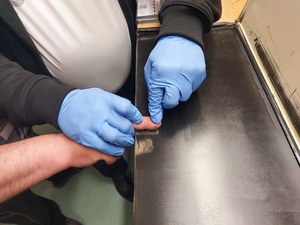 Policyjny technik kryminalistyki pobiera odciski linii papilarnych od zatrzymanego sprawcy uszkodzenia mienia