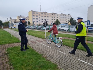Policjanci ruchu drogowego nadzorują jazdę uczestnika na rowerze w miasteczku ruchu.