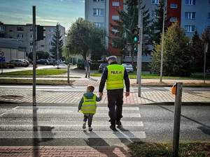 Policjant z dzieckiem przechodzący przez przejście dla pieszych.