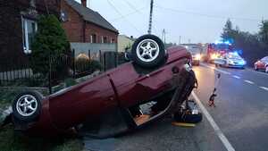 leżący na dachu samochód, w tle służby ratunkowe